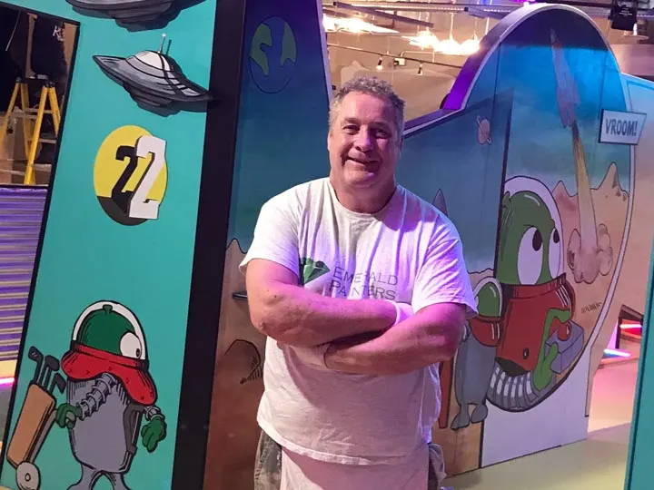 Conor McIlvenny, director of Emerald Builders, arms folded in front of a painted mural